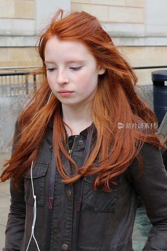 14 / 15岁的红发少女，皮肤苍白，脸上有雀斑，通过耳机听着音乐走在街上，向下看照片